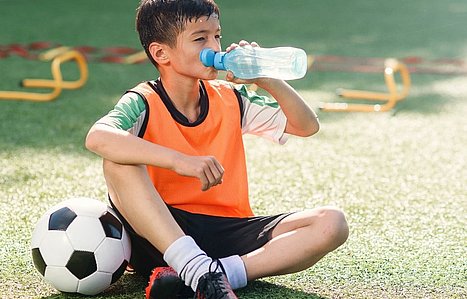 Junge in Pubertät macht Trinkpause beim Fußballtraining.