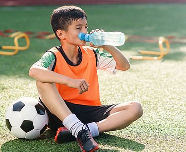 Junge in Pubertät macht Trinkpause beim Fußballtraining.