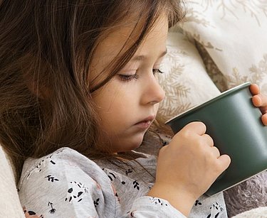 Kind mit Schluckbeschwerden trinkt eine Tasse Tee.